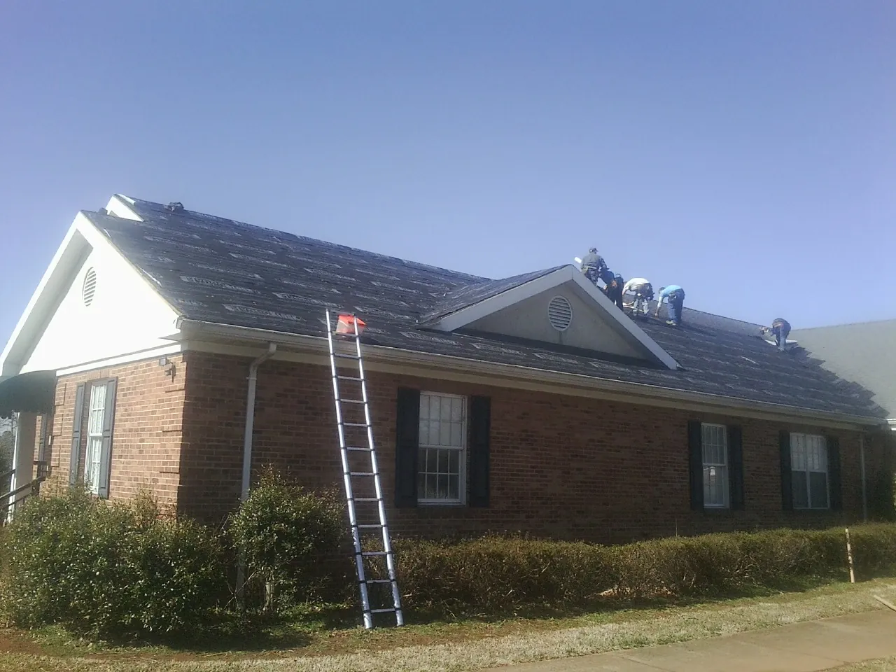 Crew tearing shingles off a brick ranch roof with a ladder set — Metal Roof Repair work by our crew in Morley