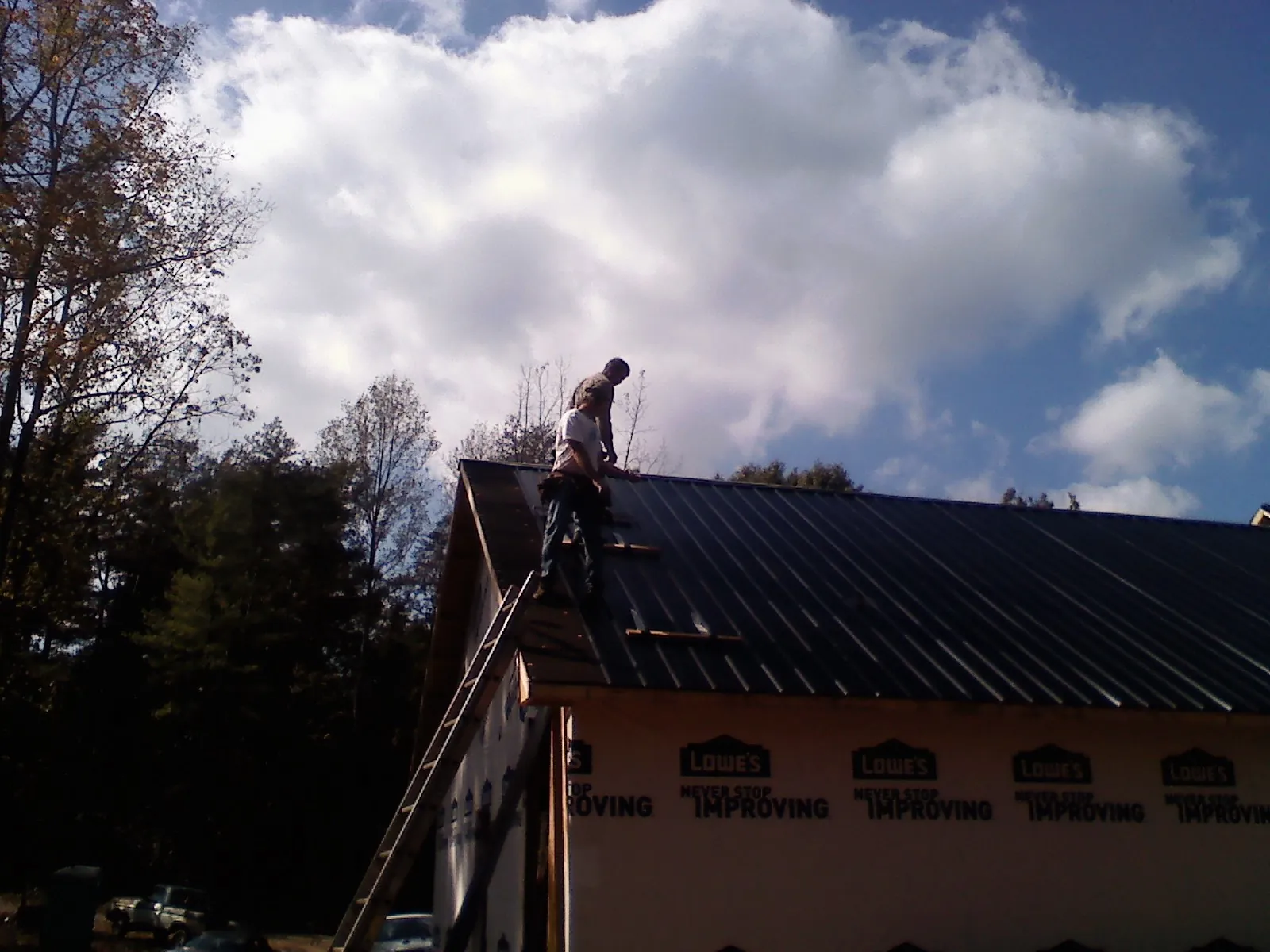 Roofer fastening dark metal panels high against a cloudy sky, from a Roof Inspection job in Morley