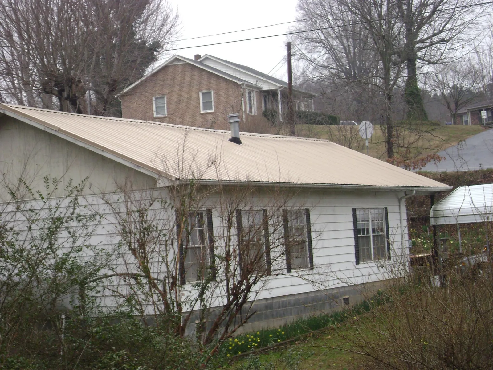 Tan metal roof on a white sided house set into a hillside — Commercial Roofing by Roofing Brothers in Morley